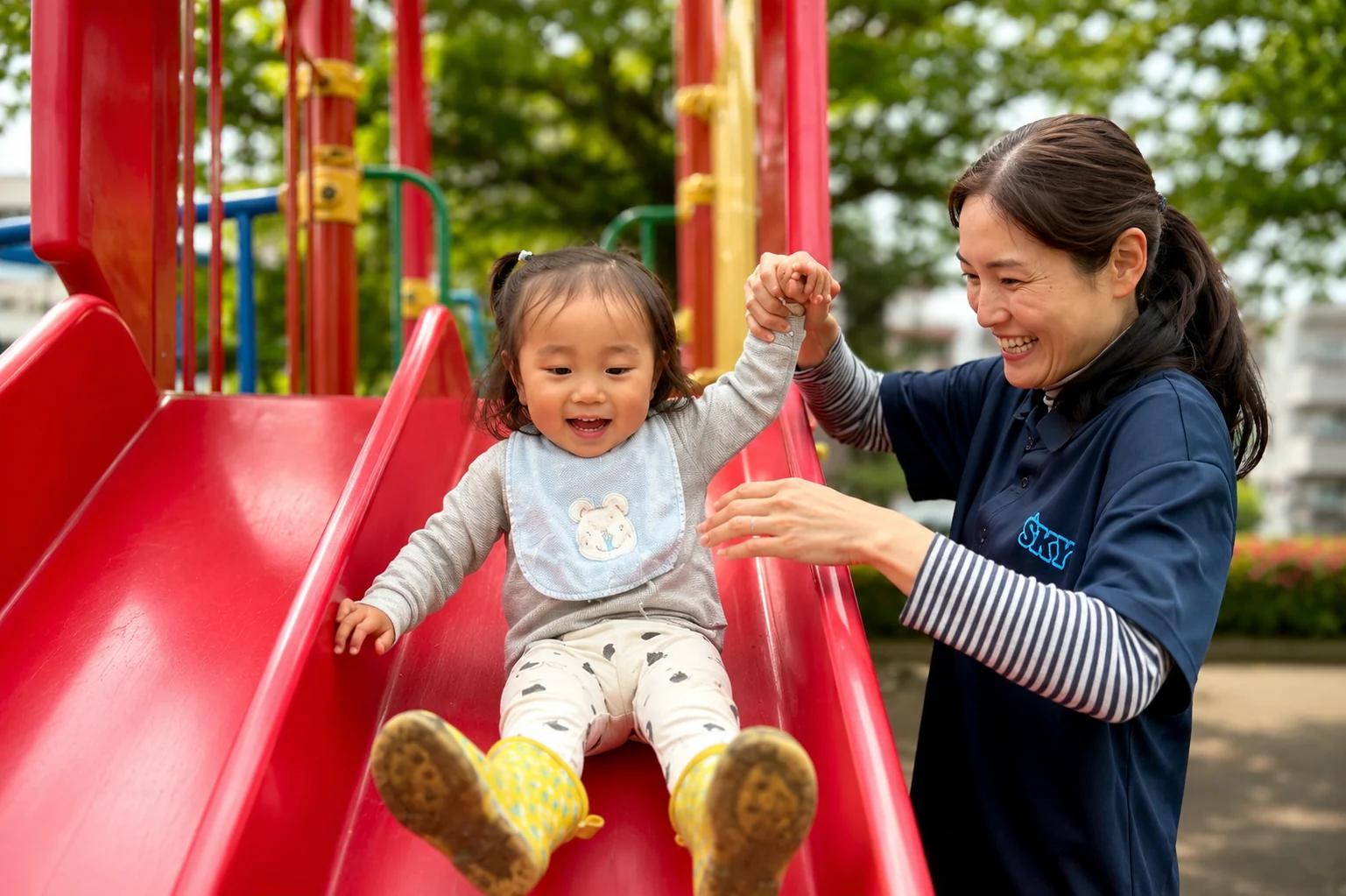 SKY保育園で先生が赤いすべり台の子どもをやさしく支えている様子